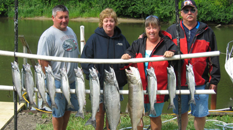 Four People Standing With Fish They Caught